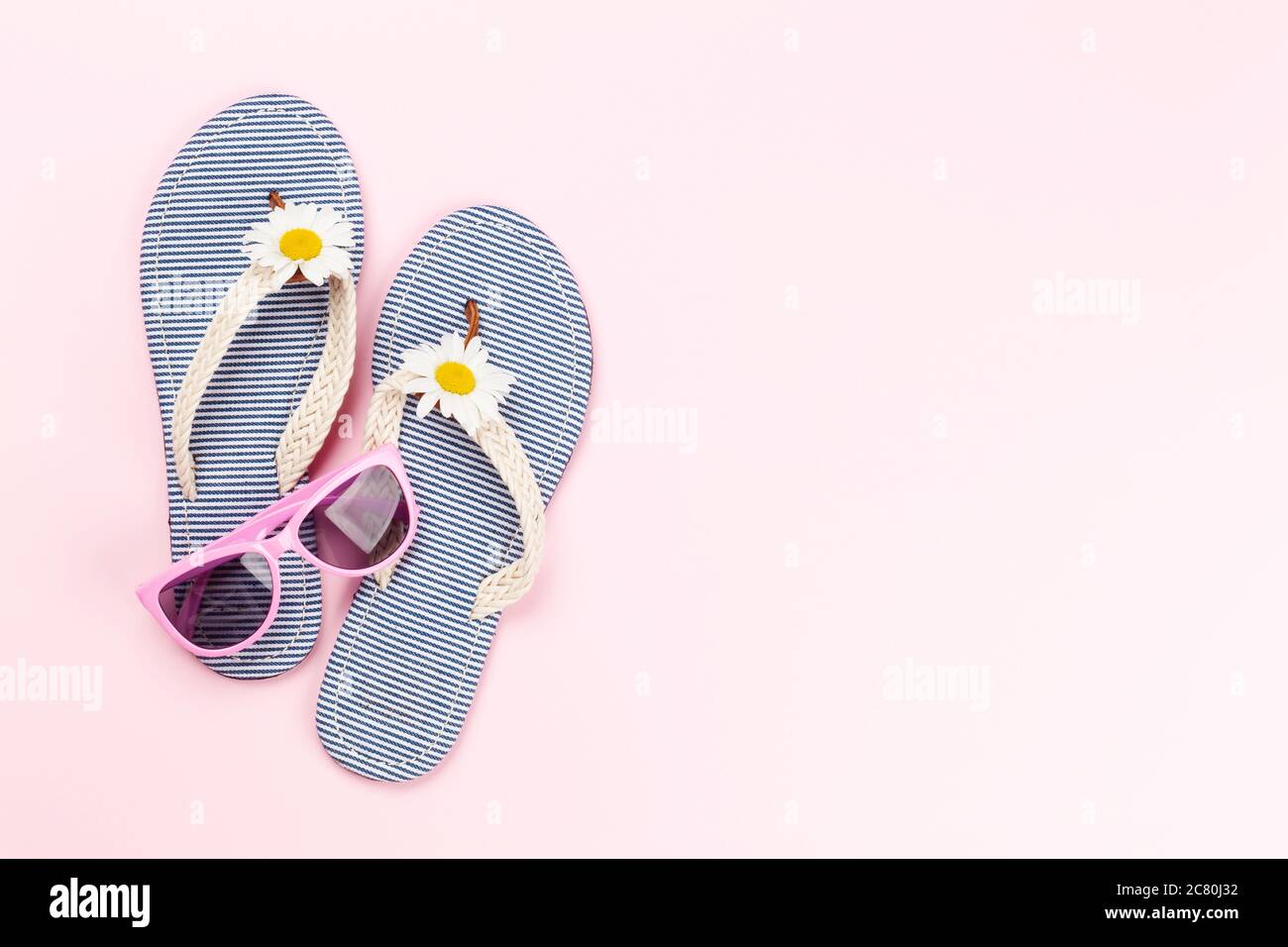 Infradito da spiaggia con fiori e occhiali da sole su sfondo rosa. Concetto di vacanza estiva. Disposizione piatta con spazio per la copia Foto Stock