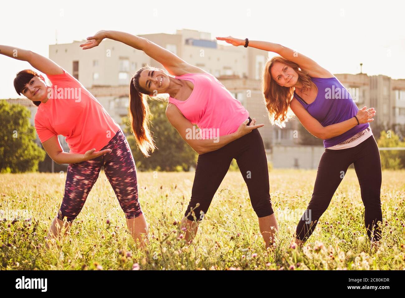 Tre giovani donne che si esercitano insieme in un parco facendo cardiovascolare laterale braccio si allunga in un sano concetto di vita attiva all'aperto Foto Stock