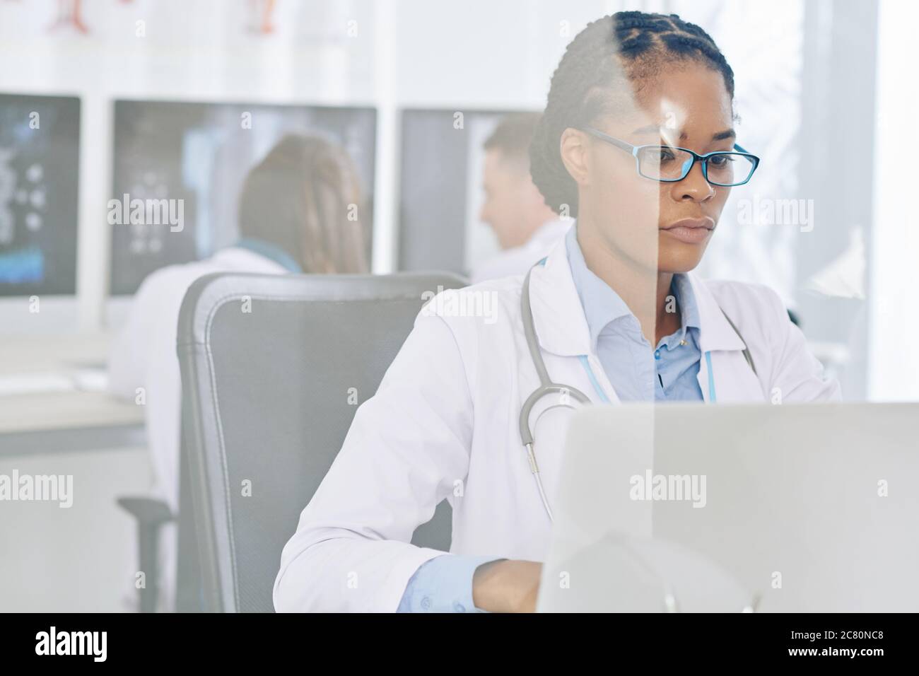 Seria giovane medico in occhiali risultati di controllo dei pazienti esami medici su computer portatile Foto Stock
