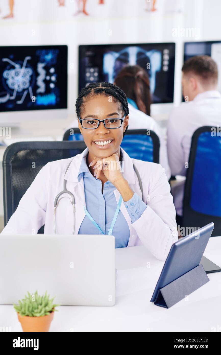 Professionista generale afro-americano sicuro e positivo seduto alla sua scrivania in laboratorio e lavorando al computer Foto Stock