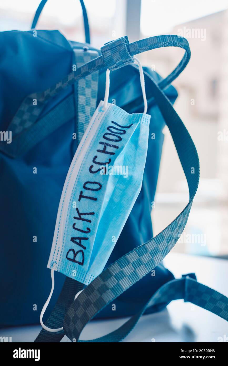 chiusura di un bookbag verde e di una maschera chirurgica blu con il testo di ritorno a scuola scritto in esso, che raffigura la necessità di prevenire l'infezione a scuola Foto Stock
