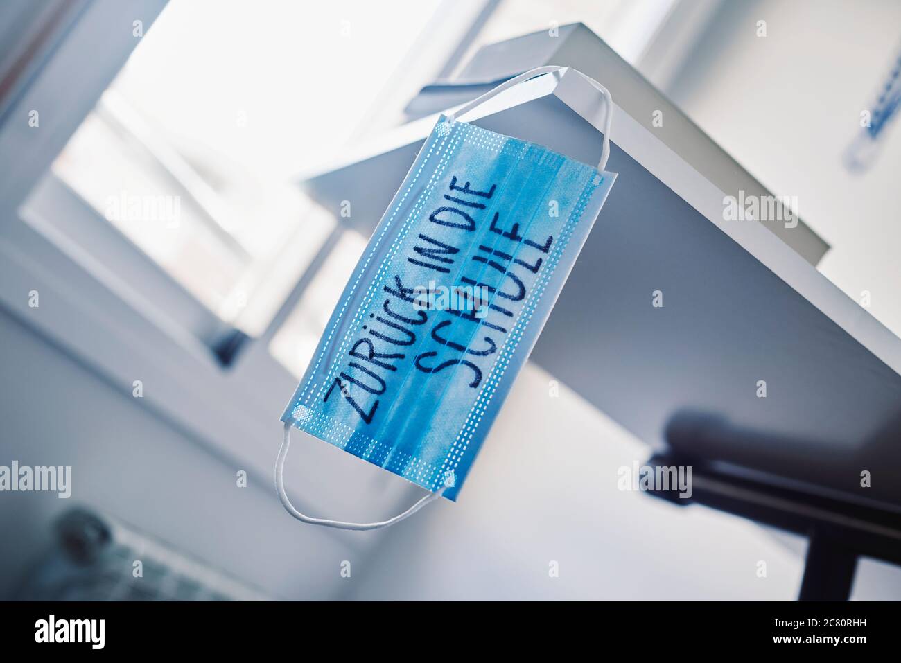 primo piano di una maschera chirurgica blu, su un tavolo, con il testo di ritorno a scuola scritto in tedesco, che raffigura la necessità di prevenire l'infezione a scuola in Foto Stock
