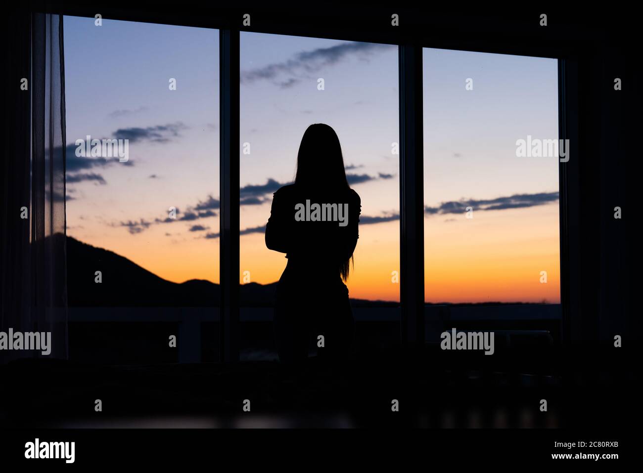 Silhouette di una donna che si trova davanti a una finestra con il tramonto sullo sfondo Foto Stock