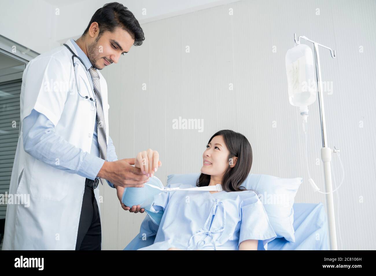Sorridente medico che esamina il braccio di una paziente femminile mentre si siede nella sala esame medico presso la clinica. Foto Stock