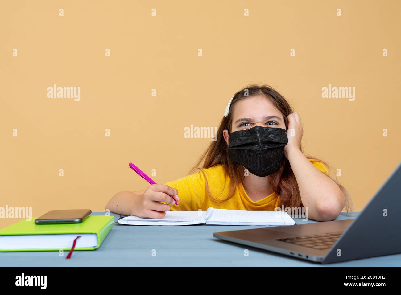 Distanza imparare formazione online. Scolaretta in maschera medica studiare a casa, lavorando al notebook portatile e facendo compiti a scuola Foto Stock