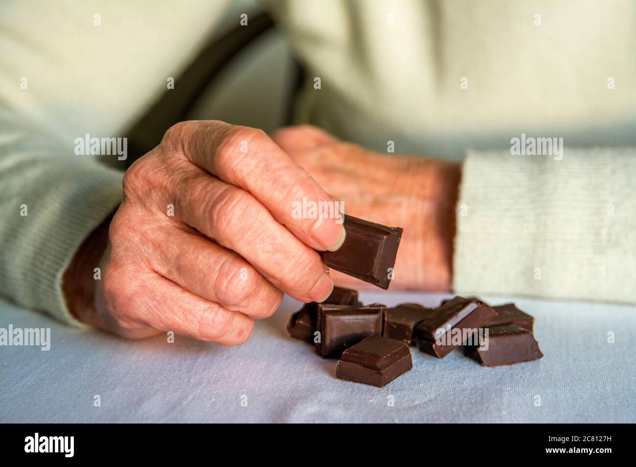 Senior che si gode di quadrati di cioccolato fondente su una superficie morbida all'interno durante un pomeriggio tranquillo Foto Stock