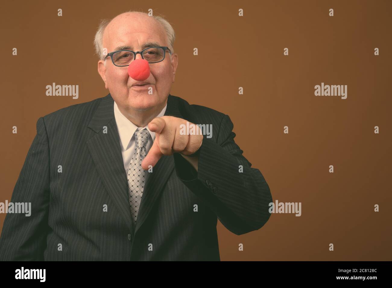 Uomo d'affari anziano in sovrappeso che indossa il naso di clown su sfondo marrone Foto Stock