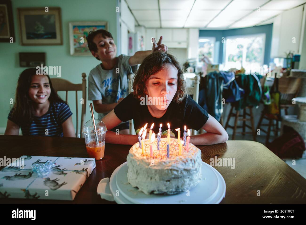 La ragazza teen soffia fuori le candele della sua torta di compleanno con fratelli vicino Foto Stock