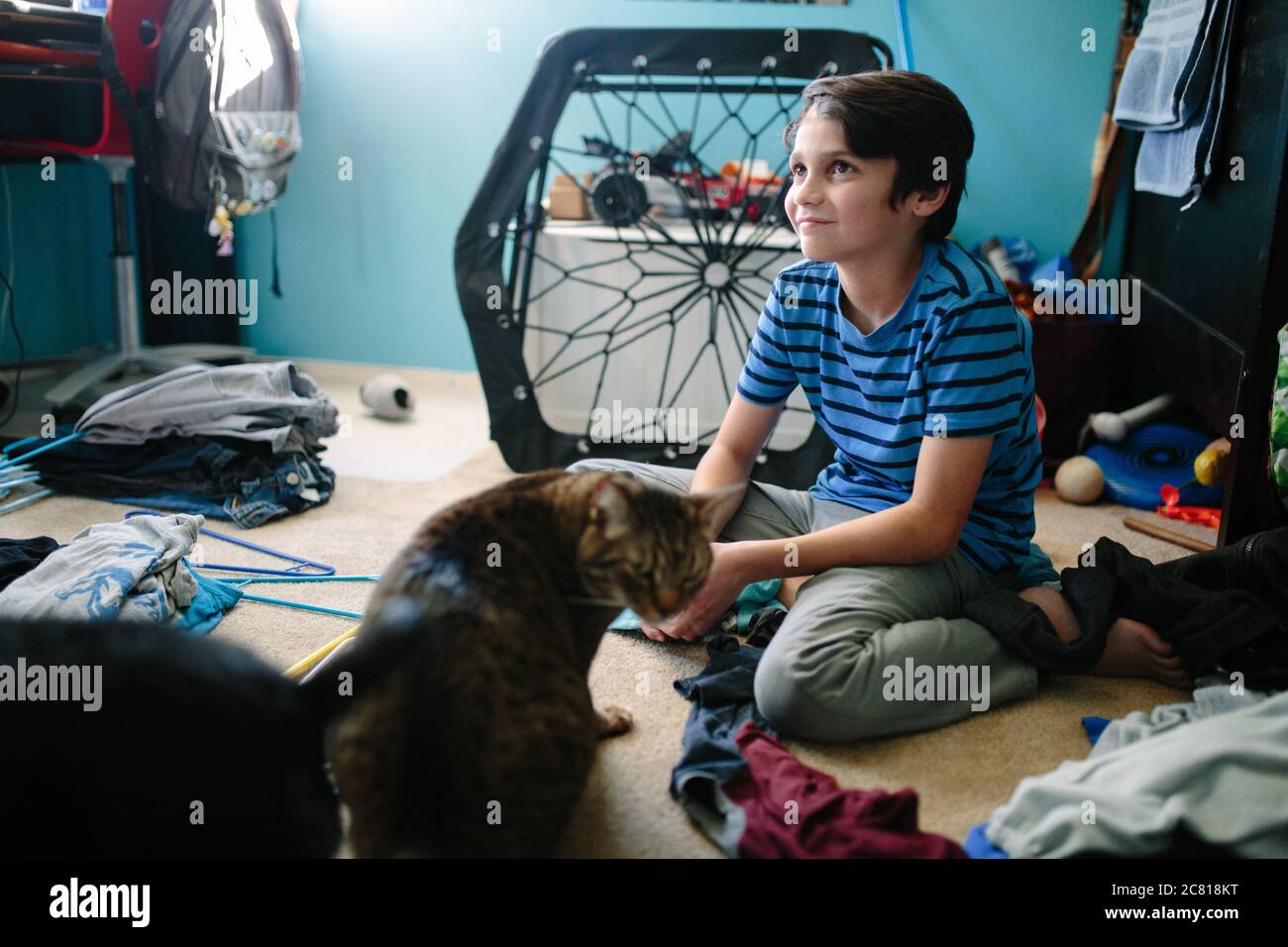 Il ragazzo di dieci anni si siede distratto accanto al suo gatto mentre facendo lavanderia Foto Stock