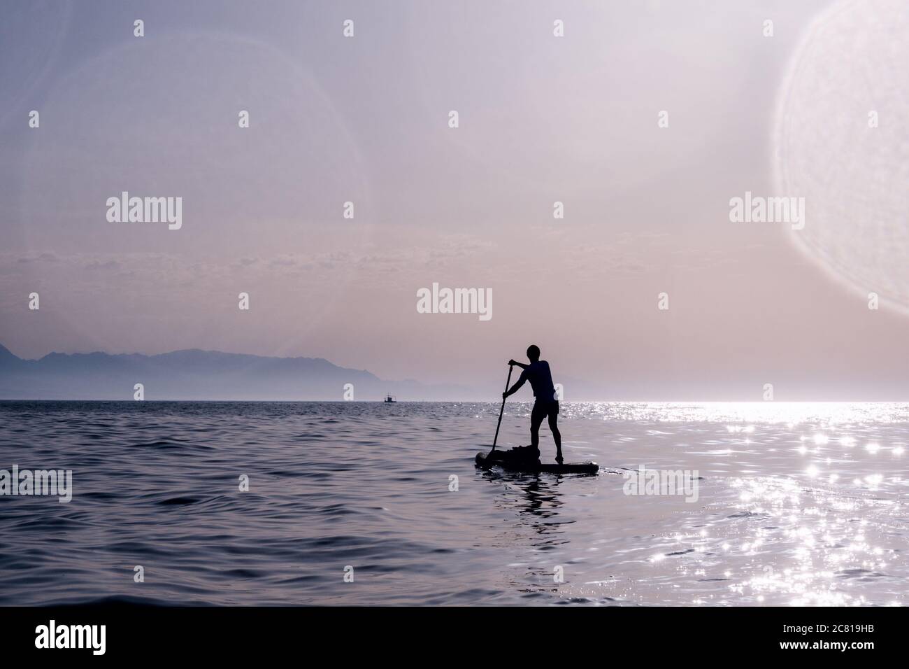 Concetto: Libertà. Silhouette di uomo che gioca in piedi su paddle. Addling nel mare all'alba. Foto Stock