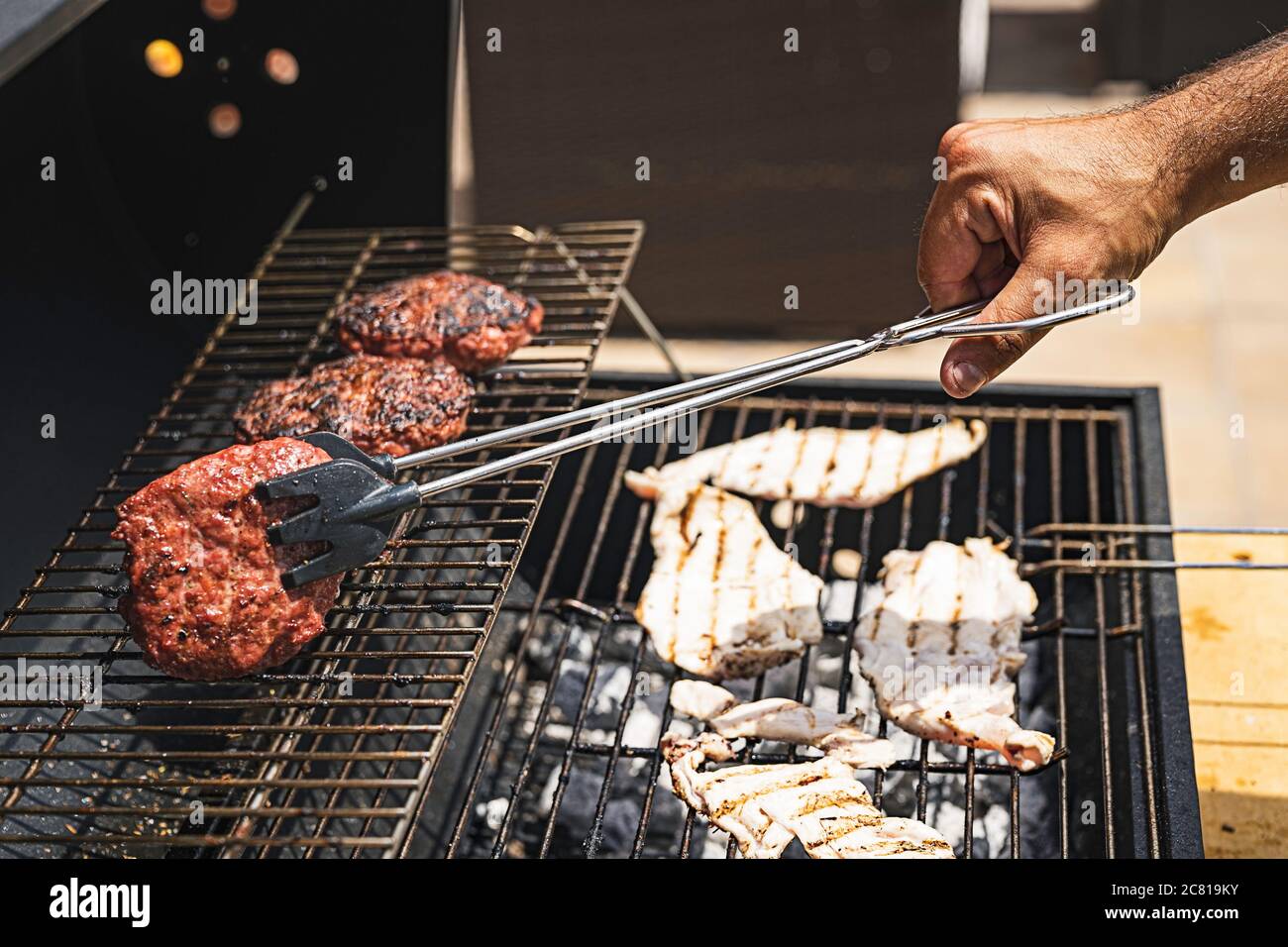 burger barbecue arrostito su grill in metallo. La persona che cucina hamburger Foto Stock