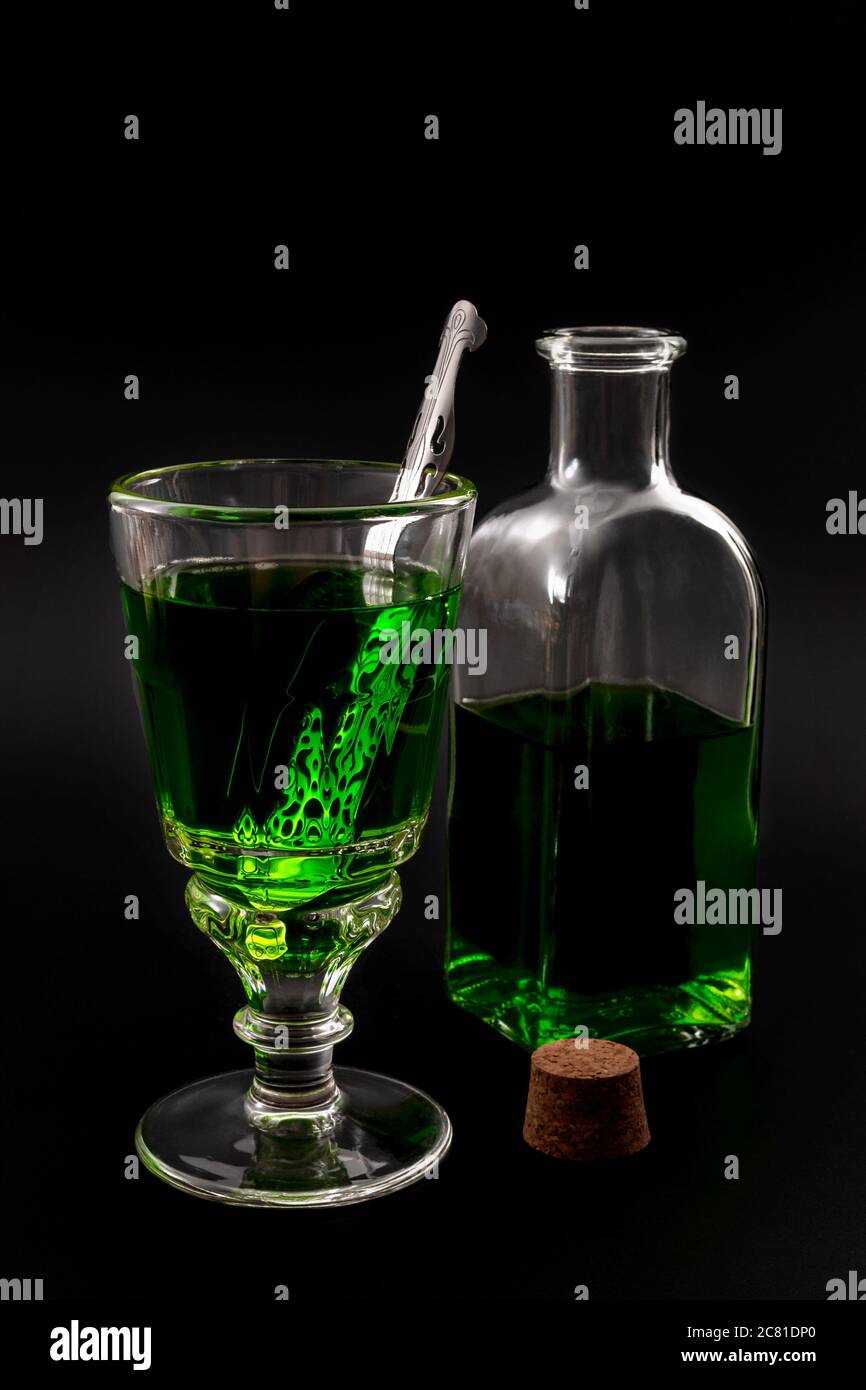 Bevanda alcolica, stimolante creativo e stile di vita bohémien con un bicchiere di assenzio verde e cucchiaio di acciaio inossidabile accanto a una bott vintage Foto Stock