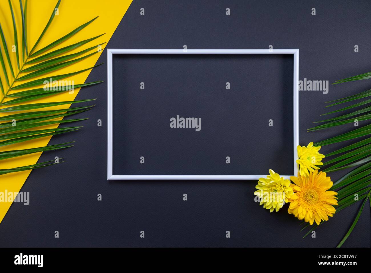 Cornice di foglie di palma tropicali e fiori su sfondo nero e giallo. Disposizione piatta, vista dall'alto, spazio per la copia. Sfondo estivo, natura. Cornice creativa ba Foto Stock