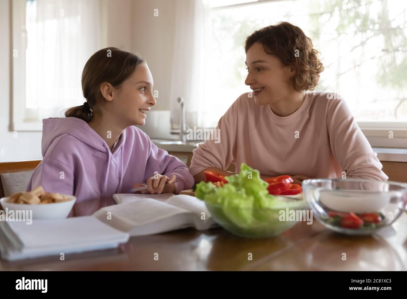 Felice madre e figlia adolescente che chiacchiera, seduto in cucina Foto Stock