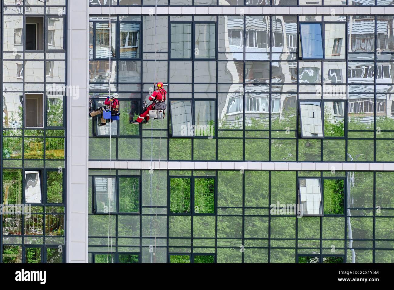 Due scalatori industriali del servizio di pulizia lavano la facciata in vetro di un alto e moderno edificio di appartamenti. Accesso tramite fune Foto Stock