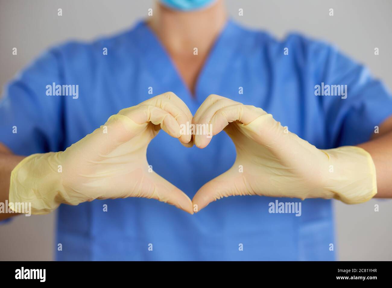 Medico o infermiere in una camicia blu rende il simbolo del cuore con le mani in guanti. Foto Stock