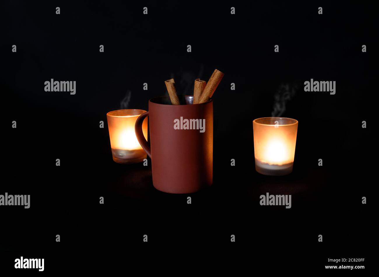 Tazza di caffè con bastoncini alla cannella in condizioni di scarsa illuminazione con vapore proveniente dalla tazza Foto Stock