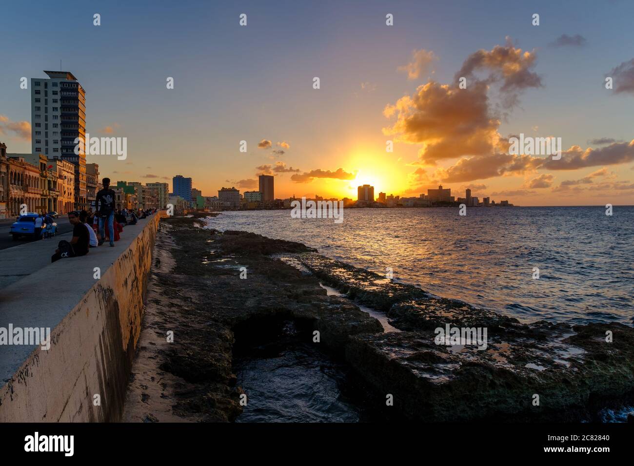 Persone sedute sulla parete di malecon a l'Avana durante un bellissimo tramonto con una vista dello skyline della città Foto Stock