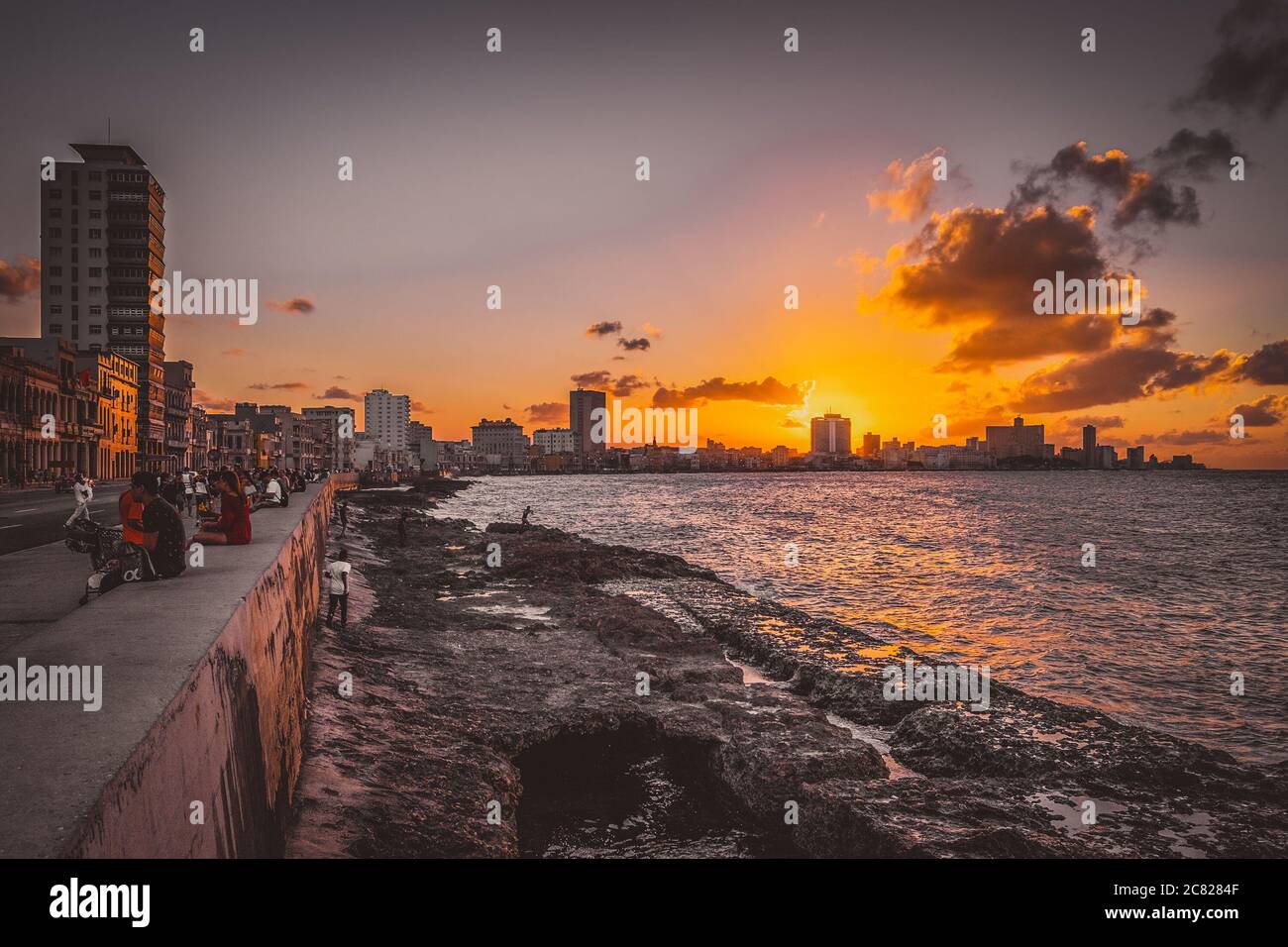 Persone sedute sulla parete di malecon a l'Avana durante un bellissimo tramonto con una vista dello skyline della città Foto Stock