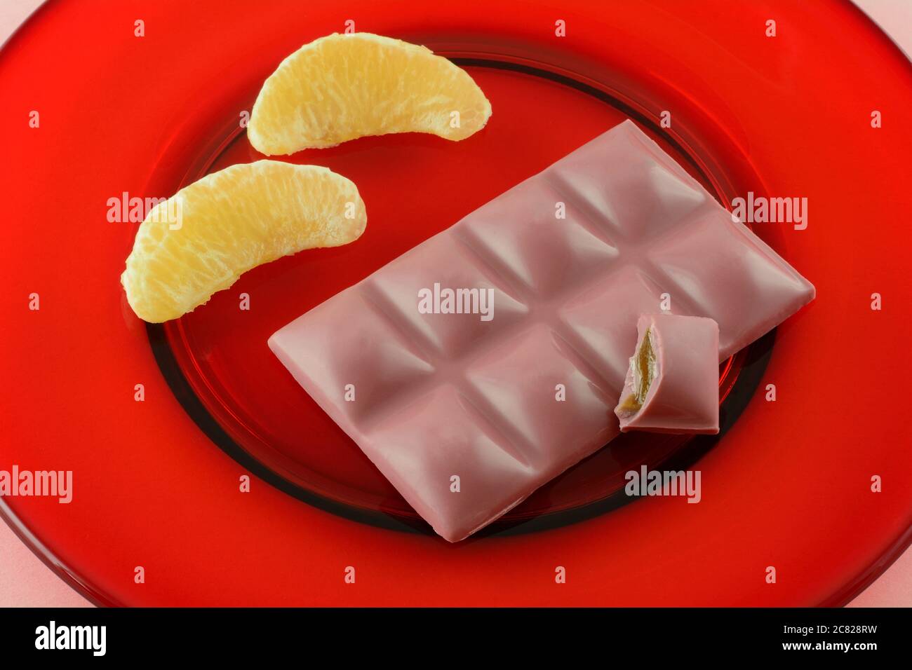 Snack bar caramelle al cioccolato con metà del pezzo consumato e sezioni di pompelmo crudo fresco su un piatto di vetro rosso Foto Stock
