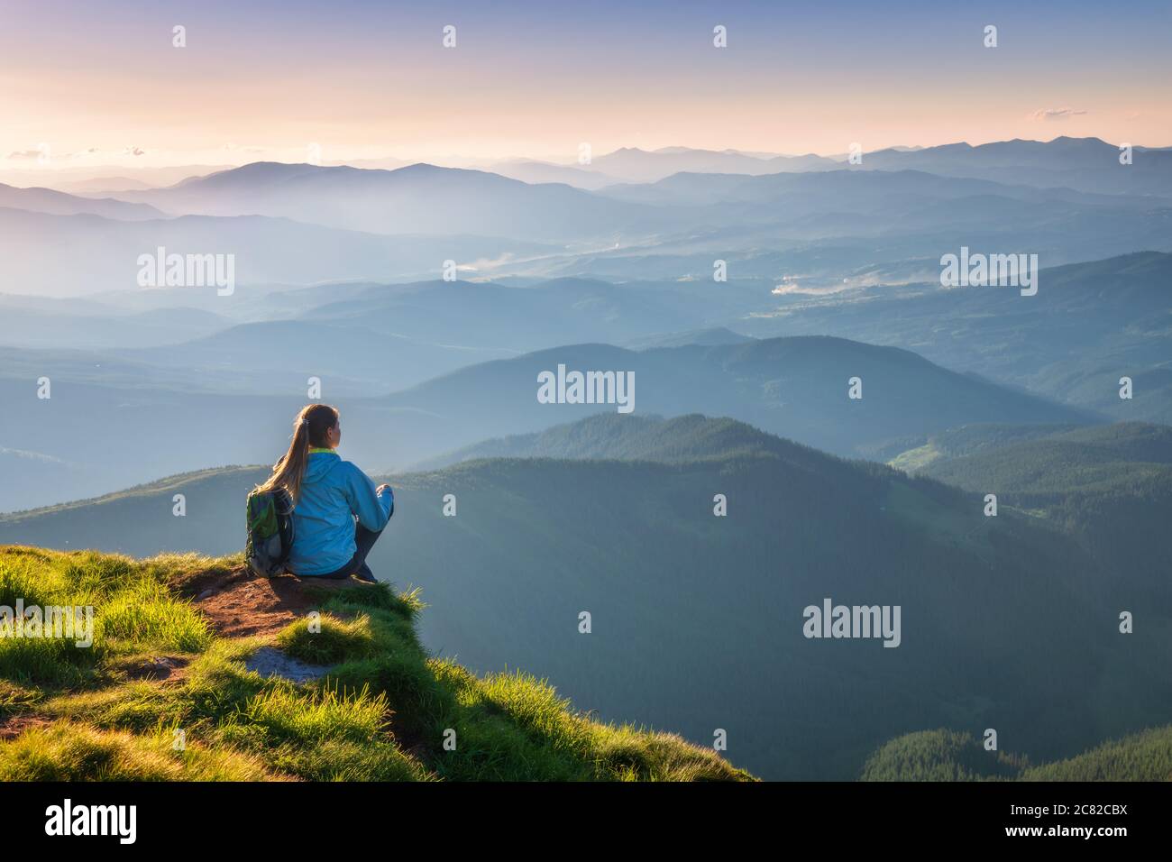 Donna con zaino seduto sulla cima della montagna al tramonto Foto Stock