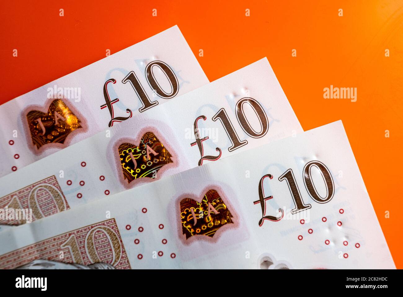 Banconote in sterline britanniche. Angoli di 10 libbre di note posizionate uno sopra l'altro sul luminoso sfondo rosso orage. Foto Stock