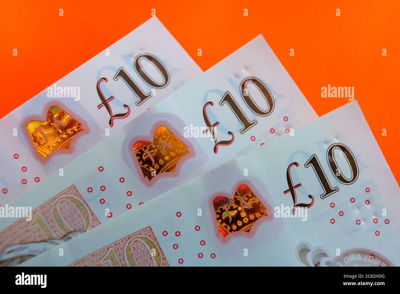 Banconote in sterline britanniche. Angoli di 10 libbre di note posizionate uno sopra l'altro sul luminoso sfondo rosso orage. Foto Stock