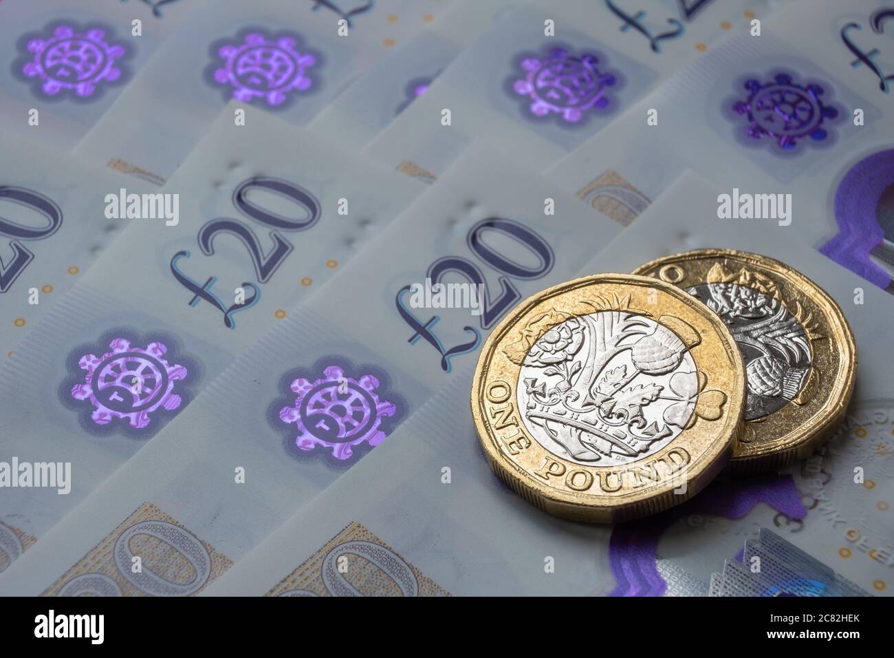 Monete nuove da una libbra poste sopra le nuove banconote inglesi in sterline. Primo piano con messa a fuoco selettiva. Il fuoco principale è sulle monete. Foto Stock