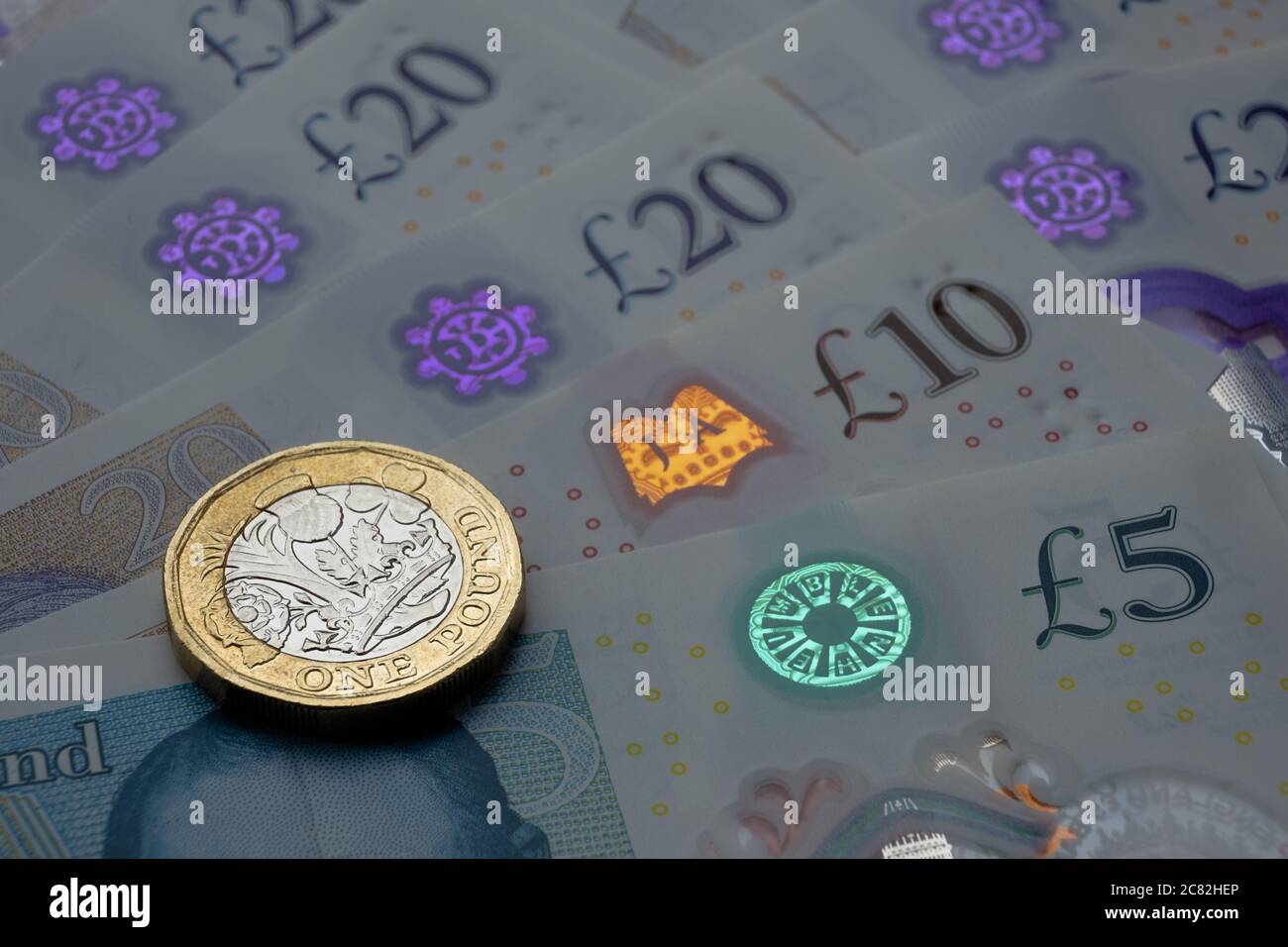 Monete inglesi da una sterlina in cima alle nuove banconote in polimero con simbolo visibile della sterlina e ologramma, Foto Stock