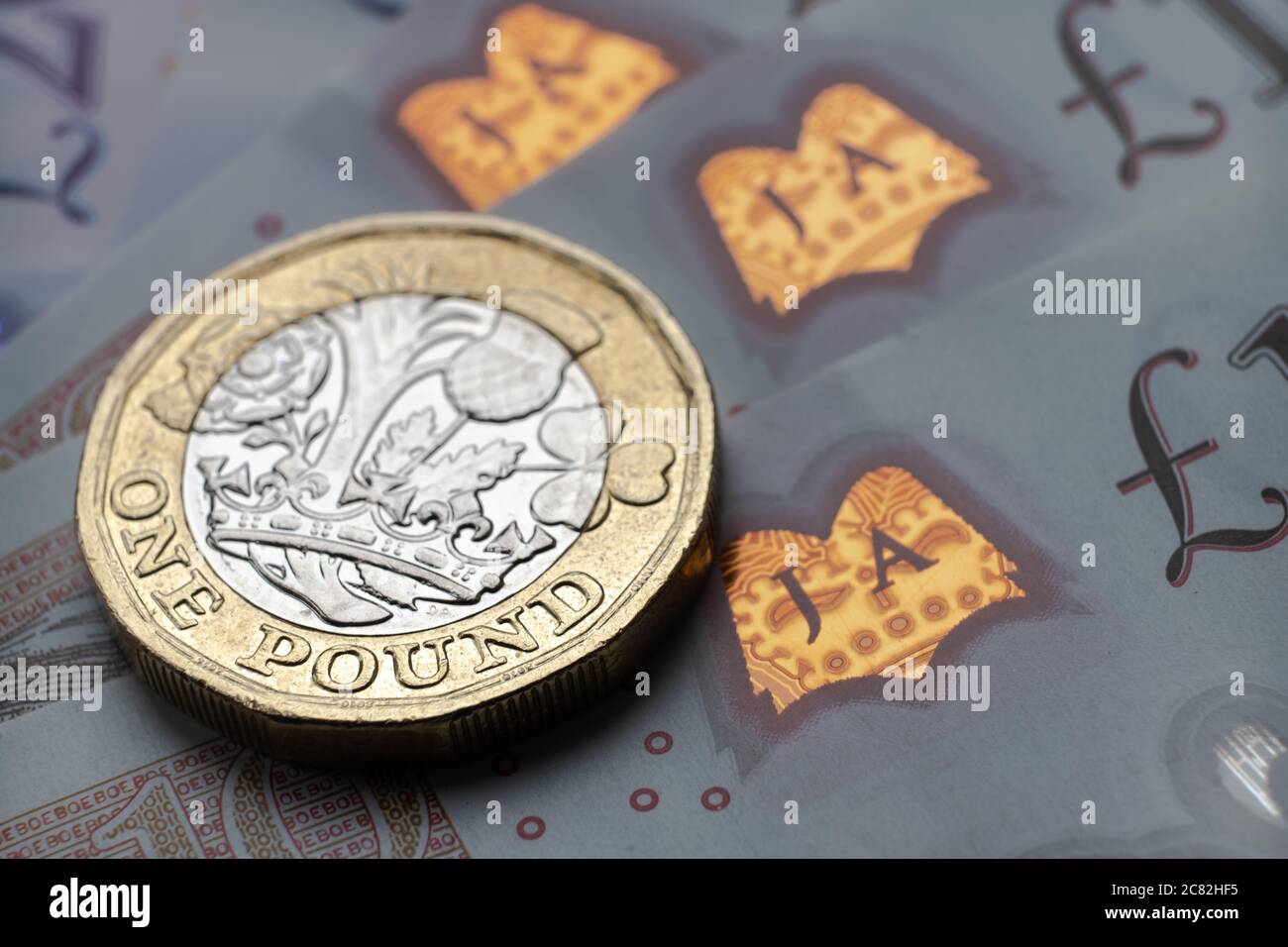Monete inglesi da una sterlina in cima alle nuove banconote in polimero con simbolo visibile della sterlina e ologramma, Foto Stock