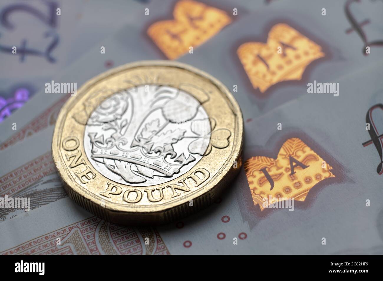 Monete inglesi da una sterlina in cima alle nuove banconote in polimero con simbolo visibile della sterlina e ologramma, Foto Stock
