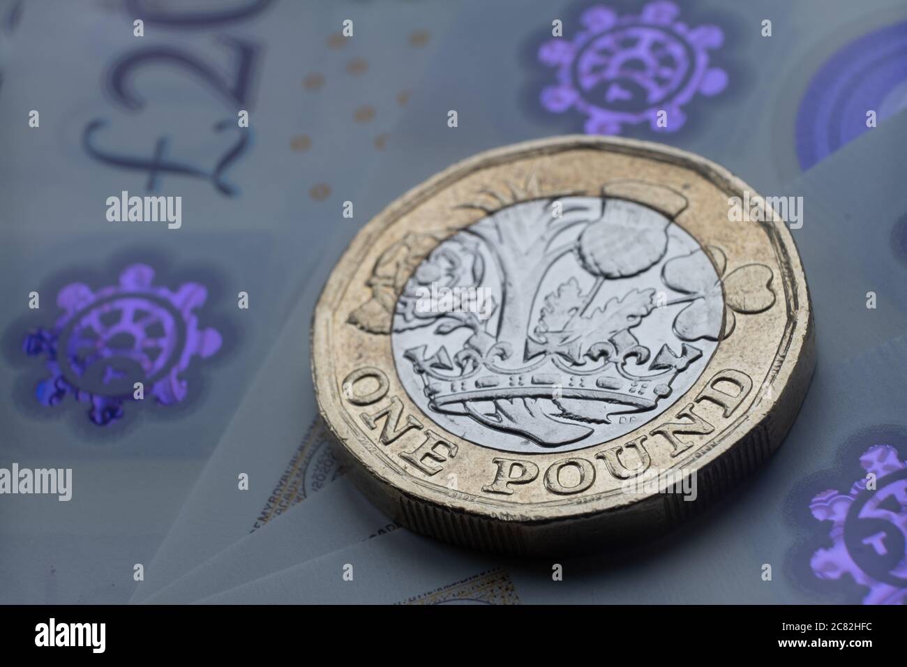 Monete inglesi da una sterlina in cima alle nuove banconote in polimero con simbolo visibile della sterlina e ologramma, Foto Stock