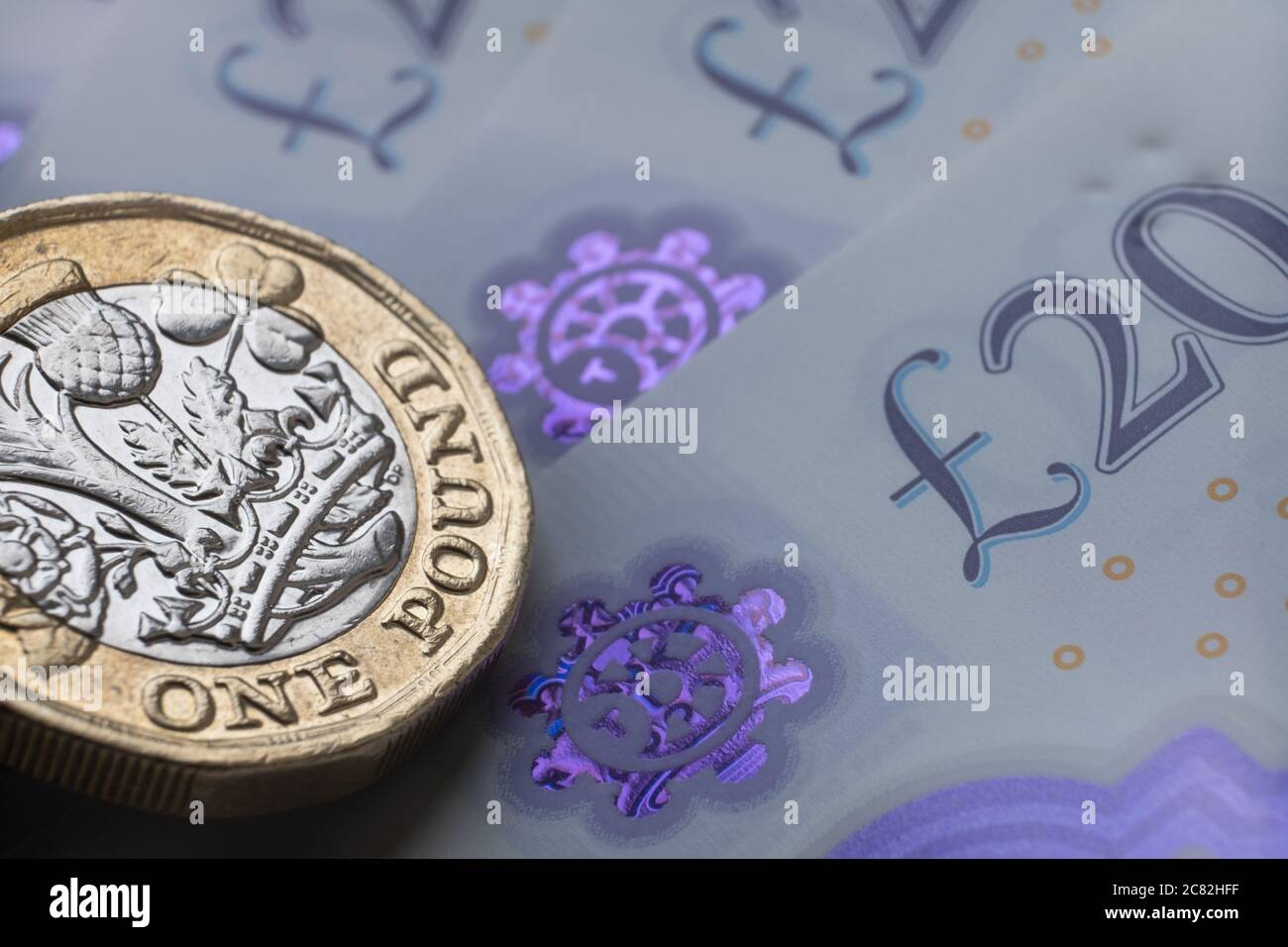 Monete inglesi da una sterlina in cima alle nuove banconote in polimero con simbolo visibile della sterlina e ologramma, Foto Stock