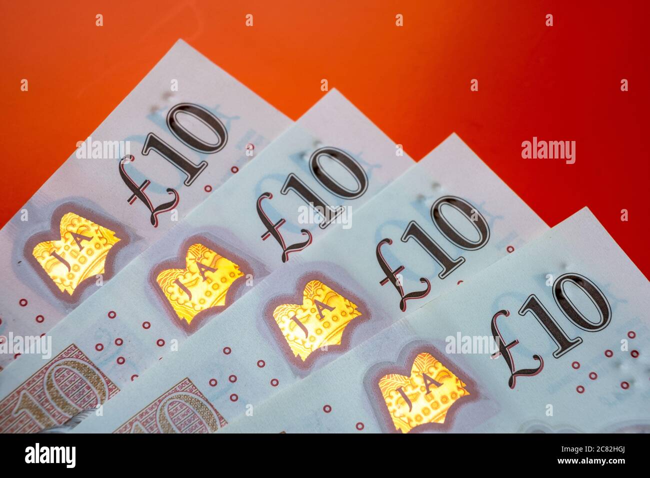 Banconote in sterline britanniche. Angoli di 10 libbre di note posizionate uno sopra l'altro sul luminoso sfondo rosso orage. Foto Stock