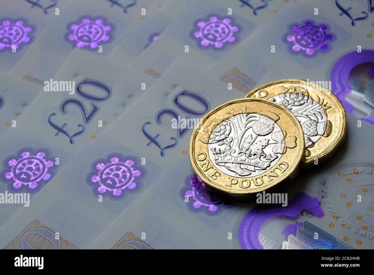 Monete nuove da una libbra poste sopra le nuove banconote inglesi in sterline. Primo piano con messa a fuoco selettiva. Il fuoco principale è sulle monete. Foto Stock