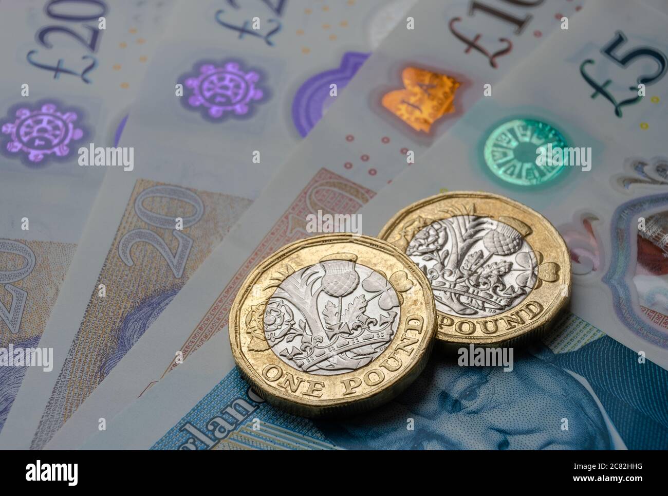 Monete nuove da una libbra poste sopra le nuove banconote inglesi in sterline. Primo piano con messa a fuoco selettiva. Il fuoco principale è sulle monete. Foto Stock