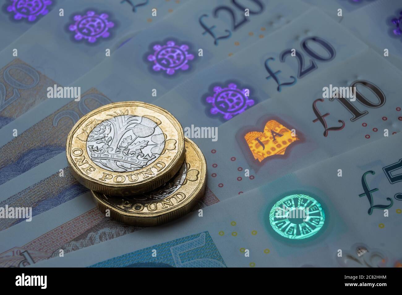Monete nuove da una libbra poste sopra le nuove banconote inglesi in sterline. Primo piano con messa a fuoco selettiva. Il fuoco principale è sulle monete. Foto Stock