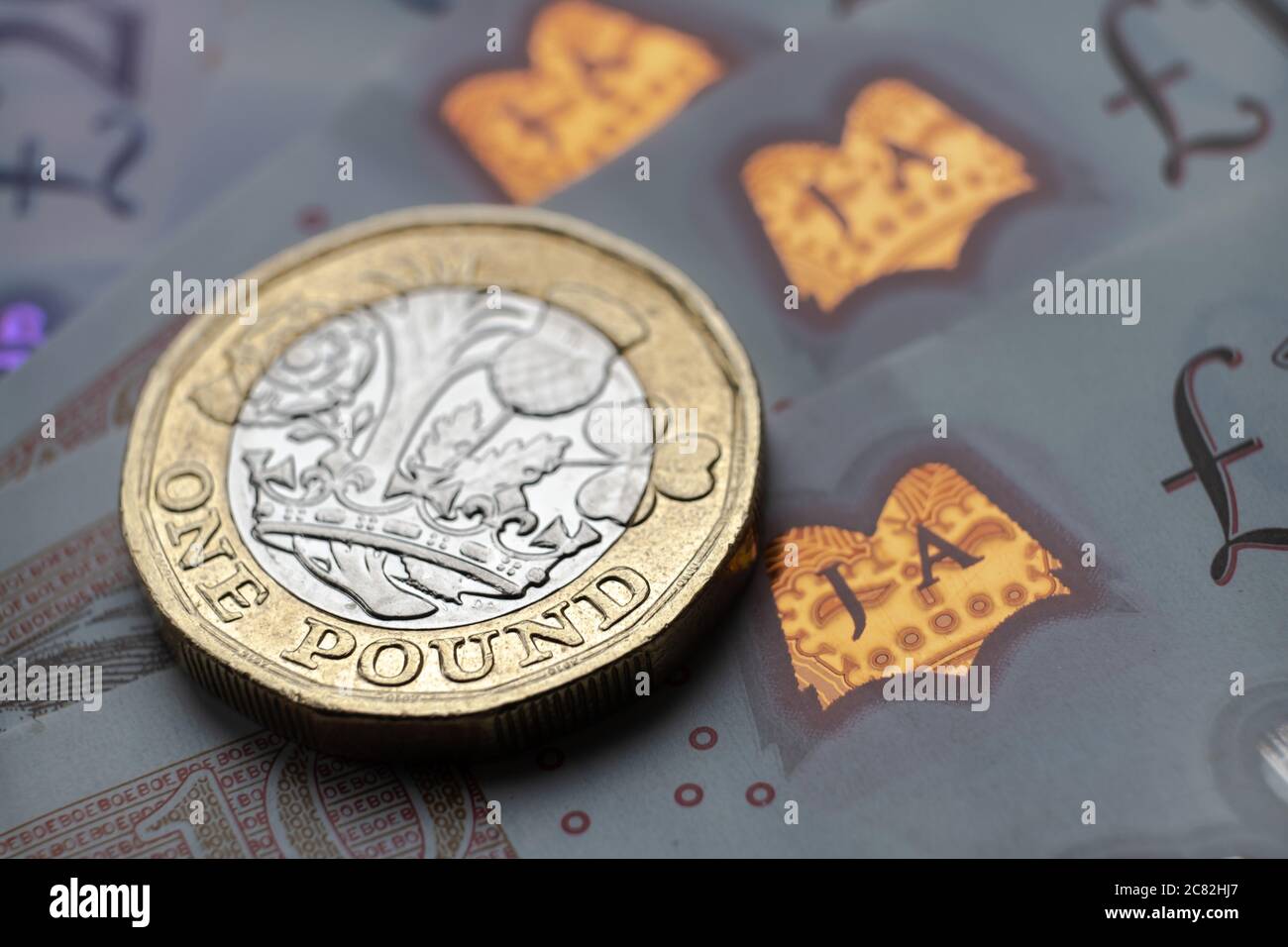 Monete inglesi da una sterlina in cima alle nuove banconote in polimero con simbolo visibile della sterlina e ologramma, Foto Stock