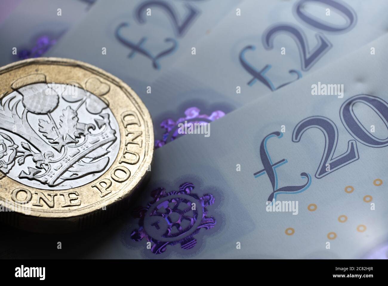 Monete inglesi da una sterlina in cima alle nuove banconote in polimero con simbolo visibile della sterlina e ologramma, Foto Stock