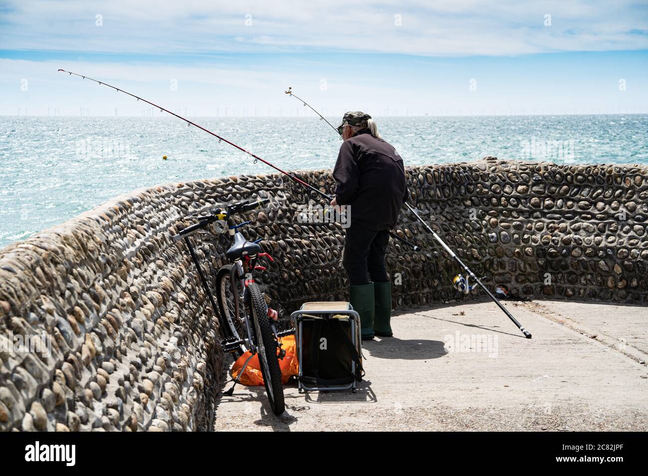 Un pescatore anziano, pesca marittima per orate di mare da una frangiflutti, Brighton, Regno Unito Foto Stock