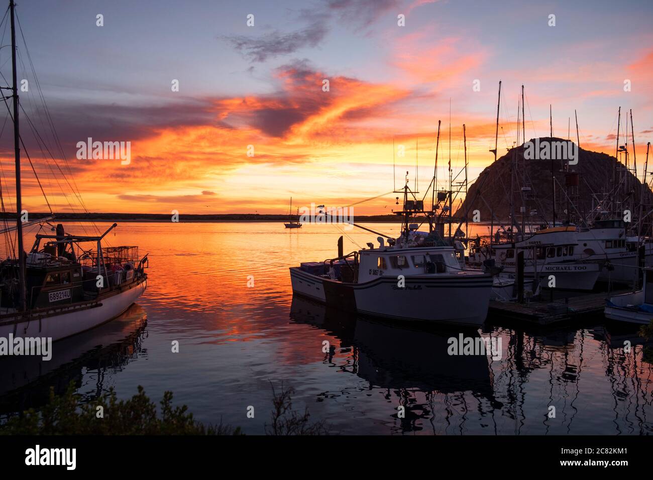 Cielo rosa fiery al tramonto sul porticciolo di Morro Bay con barche da pesca in acque calme Foto Stock