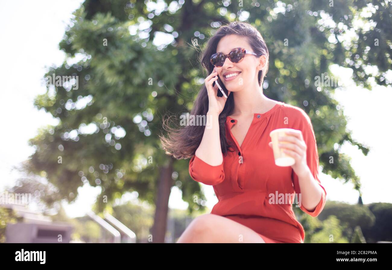 Bella donna sorridente che beve caffè mentre parla al telefono Foto Stock