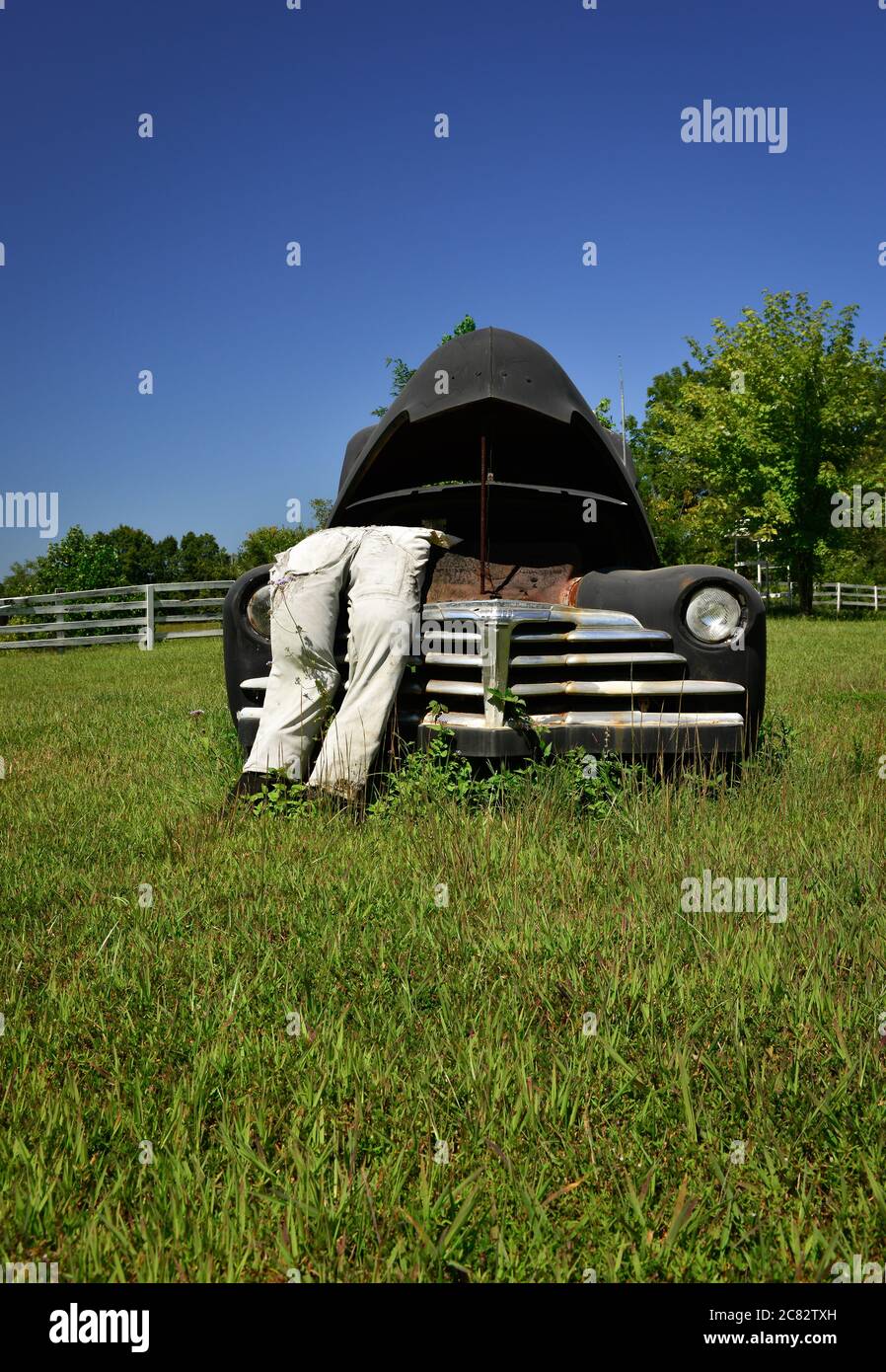 Angolo basso di una scena di città fittizia di un manichino imbottito in tute che pende in cappa schioccata su vecchia macchina degli anni '30 in campo rurale verde nel centro TN, Stati Uniti Foto Stock