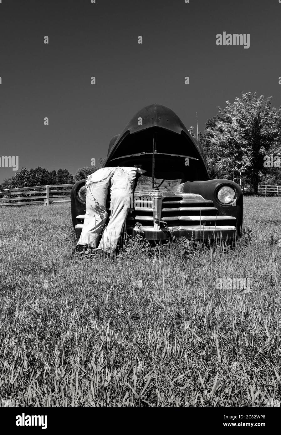 Una scena di città fittizia di un meccetto impagliato in tute si appoggia sopra il cofano schioccato su vecchia auto degli anni '30 in verde rurale nel centro TN, Stati Uniti, Foto Stock