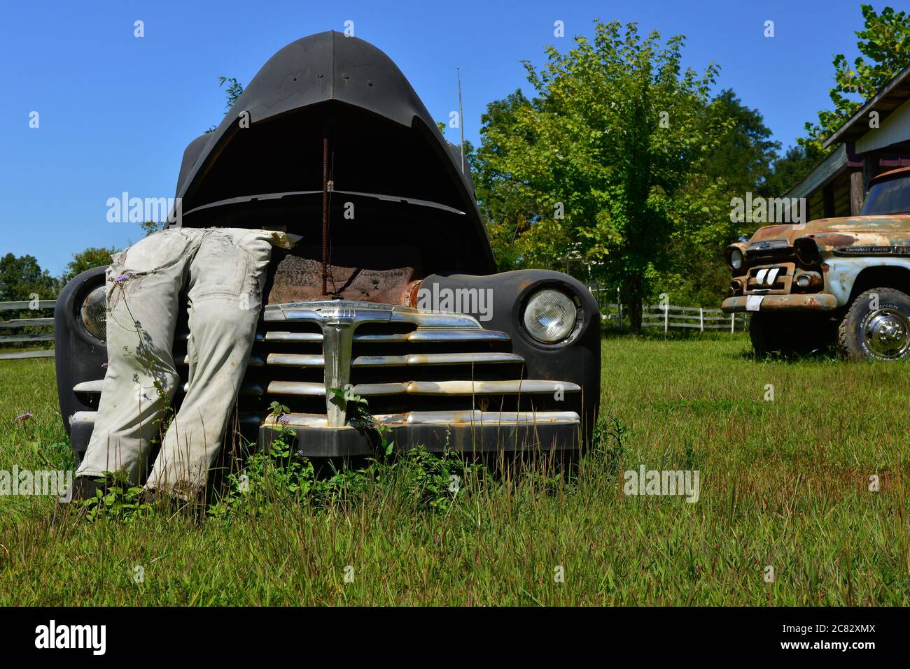 Angolo basso di una scena di città fittizia di un manichino imbottito in tute che pende in cappa schioccata su vecchia macchina degli anni '40 in campo rurale verde nel centro TN, Stati Uniti Foto Stock