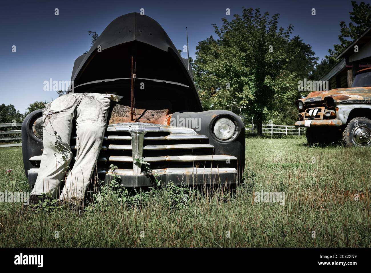 Angolo basso di una scena di città fittizia di un manichino imbottito in tute che pende in cappa schioccata su vecchia macchina degli anni '30 in campo rurale verde nel centro TN, Stati Uniti Foto Stock