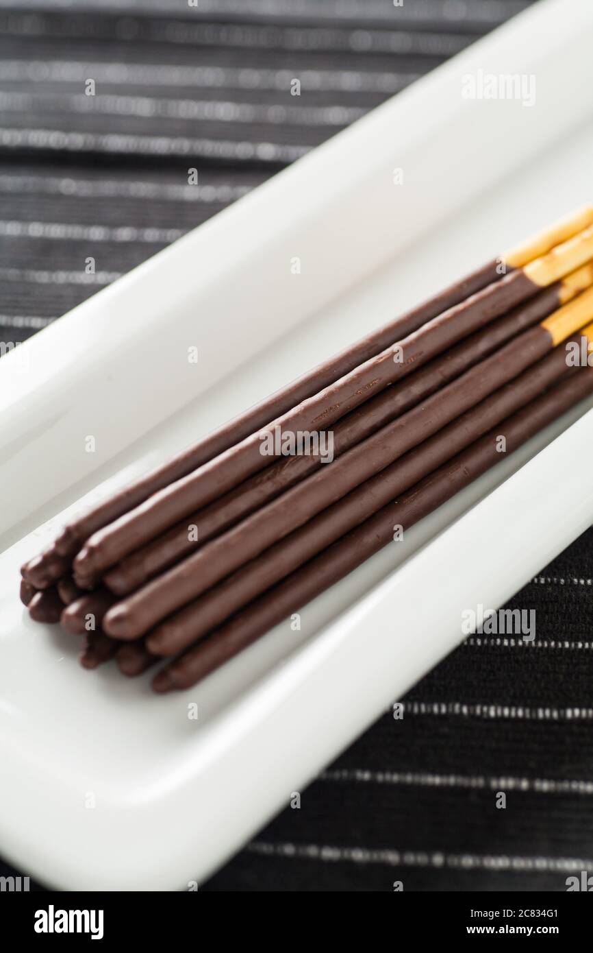 Immagine verticale di bastoncini di cioccolato Pocky posati ordinatamente su un piastra bianca lunga Foto Stock