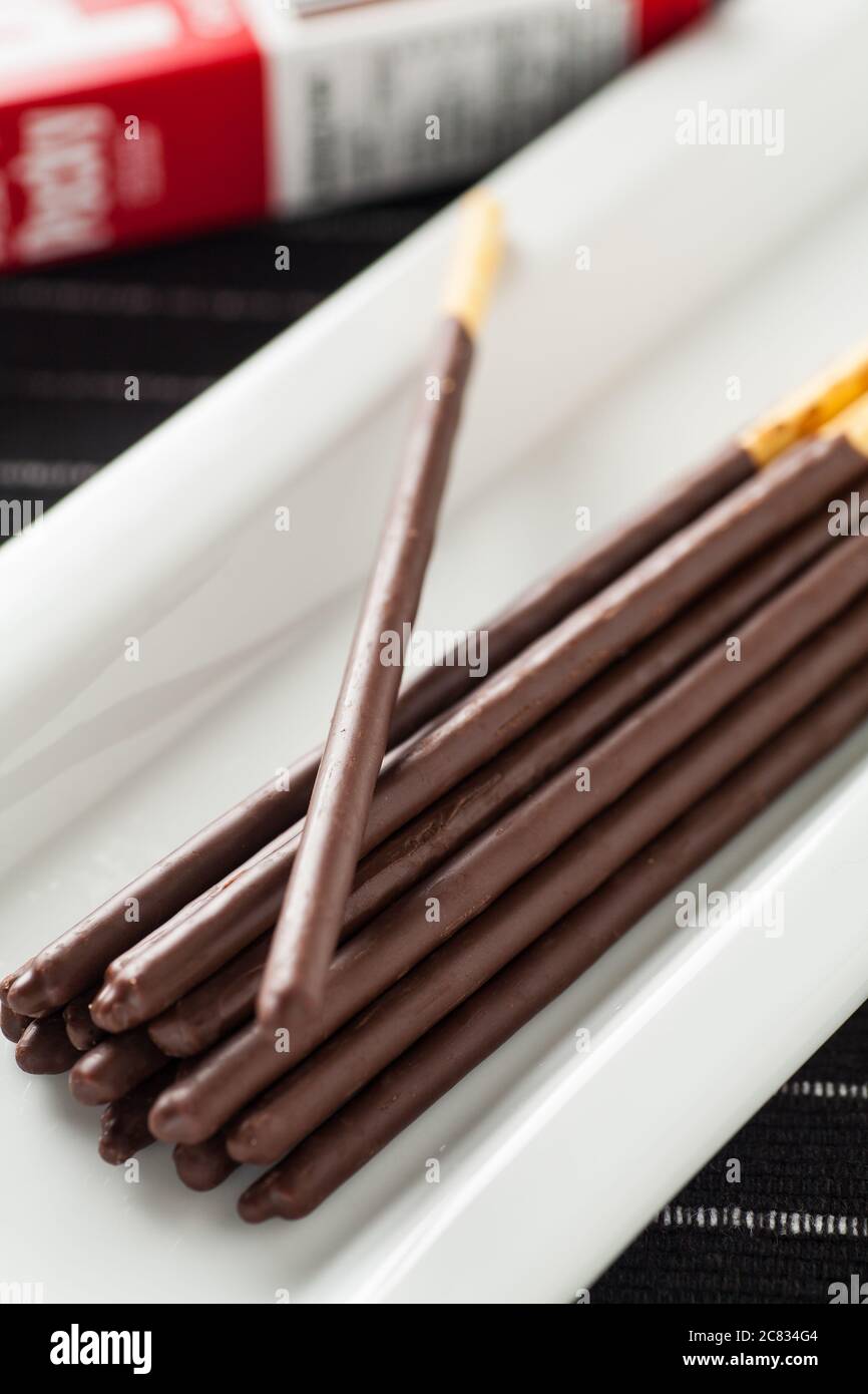Immagine verticale dei bastoncini di cioccolato Pocky su un lungo piatto bianco e confezione scatola sullo sfondo. Foto Stock