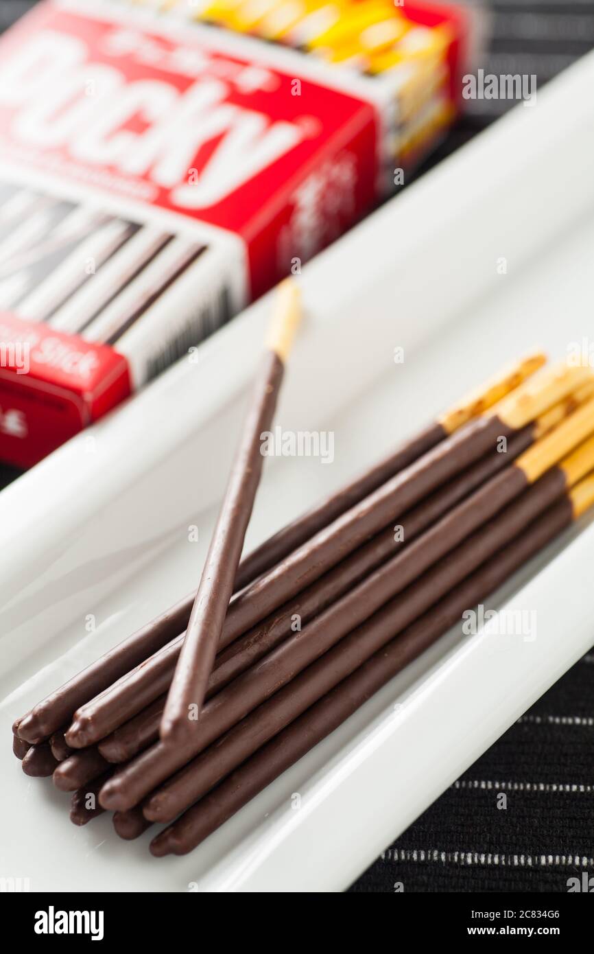Immagine verticale dei bastoncini di cioccolato Pocky su un lungo piatto bianco e sulla confezione della scatola. Foto Stock