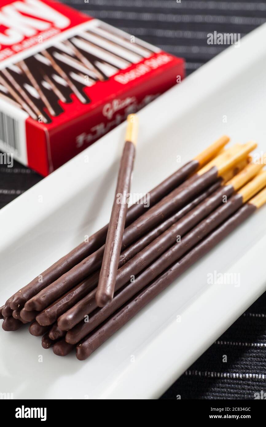 Immagine verticale dei bastoncini di cioccolato Pocky su un lungo piatto bianco e sulla confezione della scatola. Foto Stock